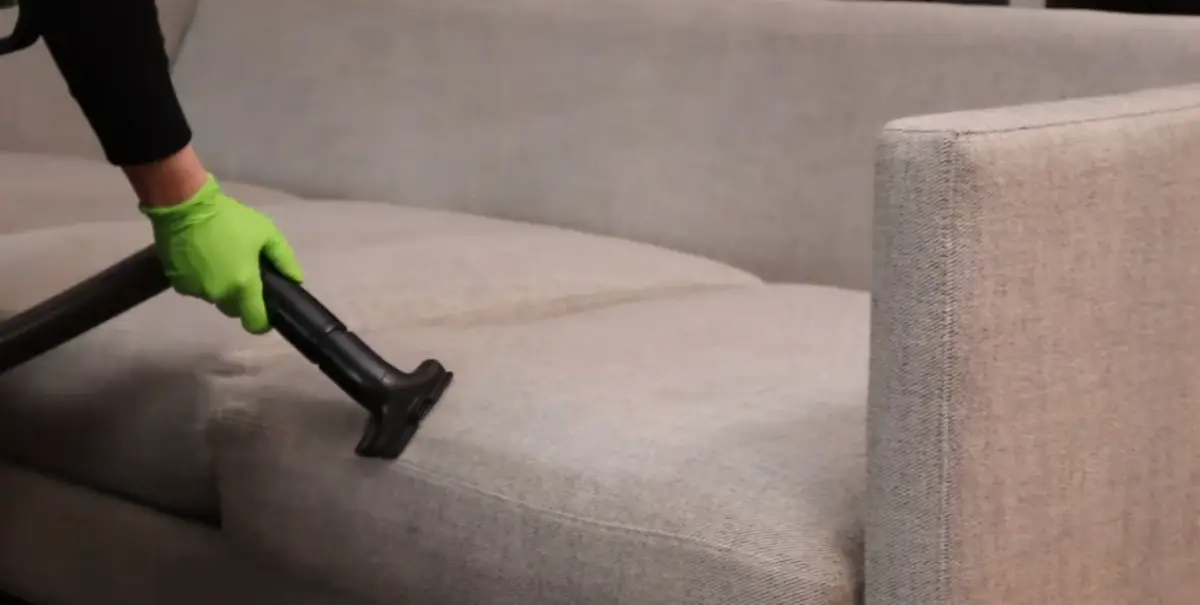 Technician vacuuming couch cushion seams before cleaning in a New York apartment