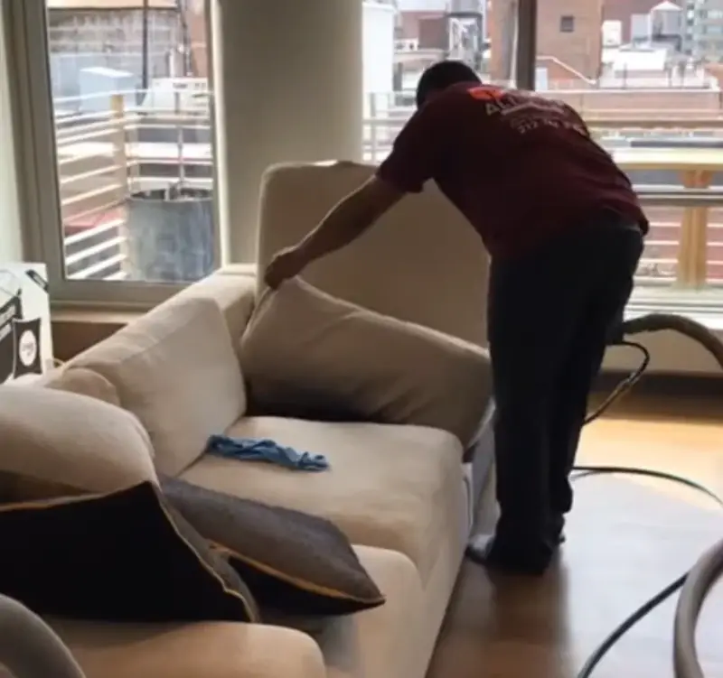 Technician lifting sofa cushions to clean underneath in a New York apartment